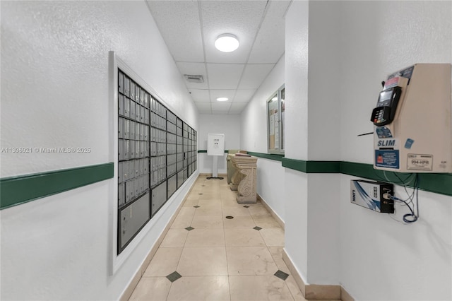 hallway featuring a paneled ceiling, visible vents, mail area, light tile patterned flooring, and baseboards