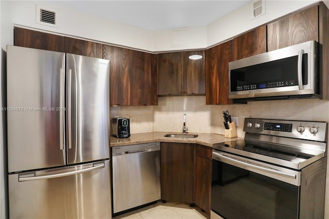 kitchen featuring light stone countertops, backsplash, stainless steel appliances, sink, and light tile patterned floors