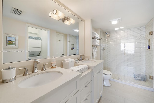 bathroom featuring tile flooring, toilet, stacked washer and clothes dryer, a shower with door, and vanity with extensive cabinet space