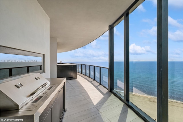 balcony featuring a view of the beach, area for grilling, an outdoor kitchen, and a water view