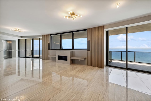 unfurnished living room with a water view, light tile floors, french doors, and an inviting chandelier