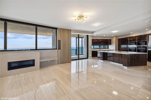 kitchen with a kitchen bar, a water view, light tile floors, a kitchen island, and dark brown cabinets