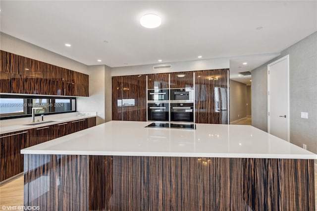 kitchen with double oven, a center island, multiple ovens, black electric stovetop, and sink