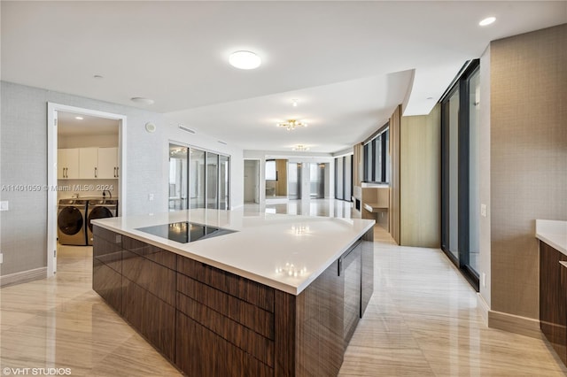 kitchen featuring washer and dryer, a center island with sink, light tile floors, and black electric stovetop