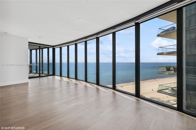 spare room featuring a view of the beach, expansive windows, wood-type flooring, and a water view