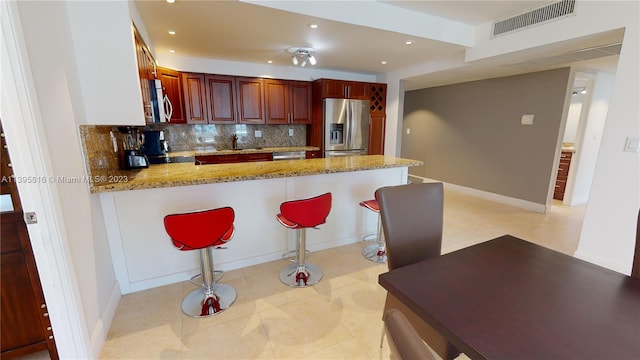 kitchen featuring light stone counters, a kitchen breakfast bar, appliances with stainless steel finishes, light tile flooring, and tasteful backsplash