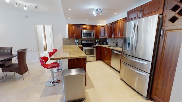 kitchen featuring kitchen peninsula, sink, appliances with stainless steel finishes, light stone countertops, and tasteful backsplash