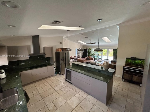 kitchen with pendant lighting, wall chimney range hood, ceiling fan, wine cooler, and stainless steel fridge