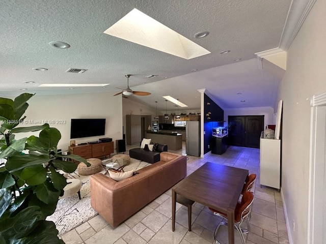 tiled living room featuring lofted ceiling with skylight, a textured ceiling, crown molding, and ceiling fan