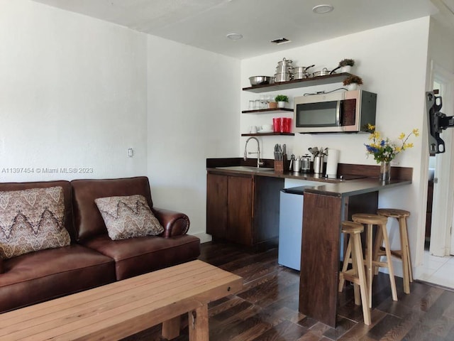 bar with dark brown cabinets, dark wood-type flooring, and sink