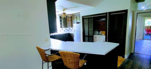 kitchen with white refrigerator, a kitchen bar, ceiling fan, kitchen peninsula, and hardwood / wood-style floors