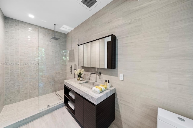 bathroom with vanity, a tile shower, toilet, and tile walls