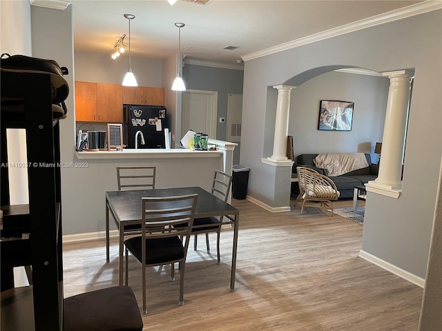 dining room with crown molding, decorative columns, and light wood-type flooring