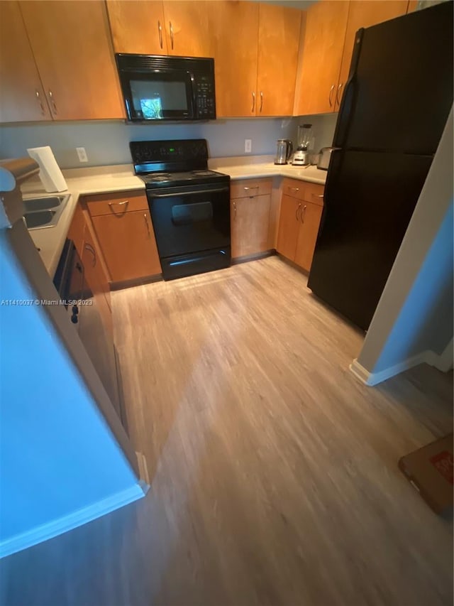 kitchen with light wood-type flooring, black appliances, and sink