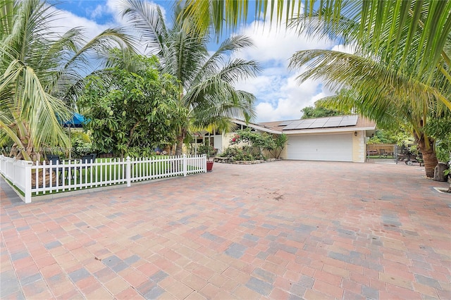 view of front of house featuring a garage, fence private yard, roof mounted solar panels, and decorative driveway