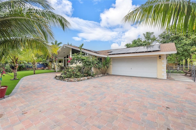 view of front of property with an attached garage, roof mounted solar panels, and decorative driveway