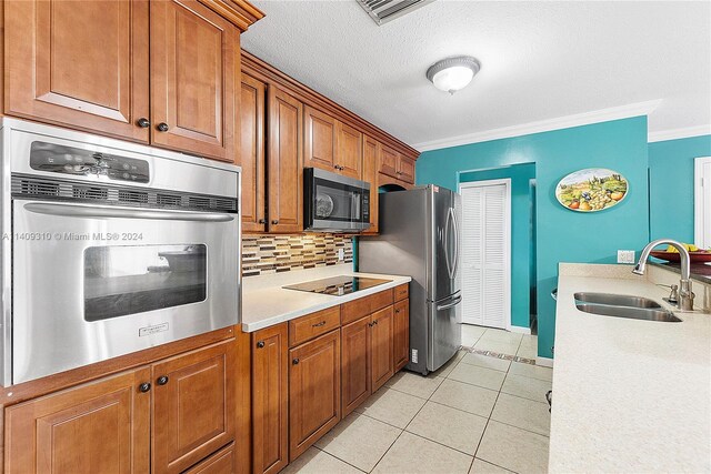 kitchen featuring crown molding, tasteful backsplash, light tile patterned floors, stainless steel appliances, and sink