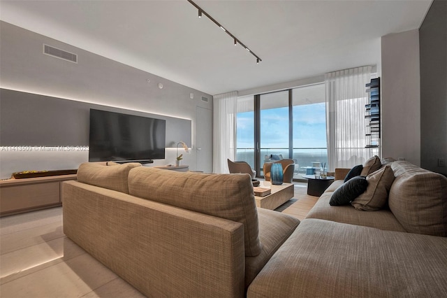 living room with a water view, floor to ceiling windows, light tile floors, and rail lighting