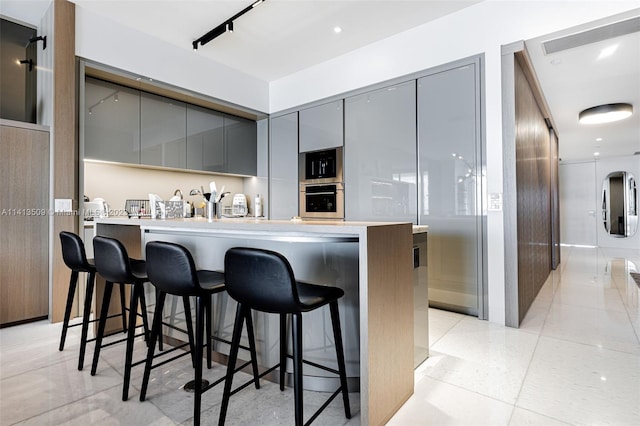 kitchen featuring oven, light tile floors, a kitchen breakfast bar, and gray cabinets