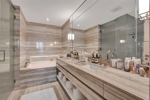 bathroom with independent shower and bath, tile walls, large vanity, and double sink