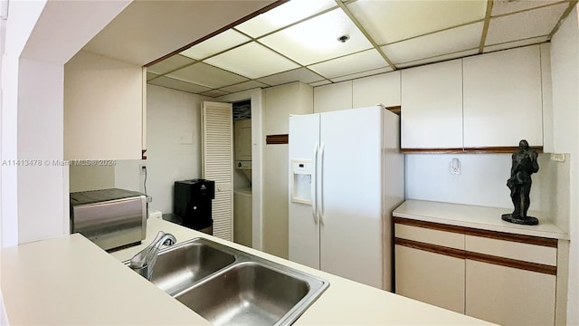 kitchen with stacked washer / dryer, white refrigerator with ice dispenser, a paneled ceiling, sink, and white cabinetry