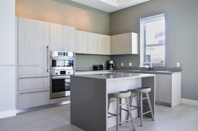 kitchen featuring stainless steel double oven, light hardwood / wood-style floors, a kitchen island, and a breakfast bar