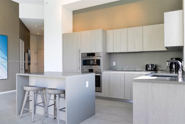 kitchen featuring a kitchen island, a breakfast bar, light hardwood / wood-style flooring, double oven, and black electric cooktop