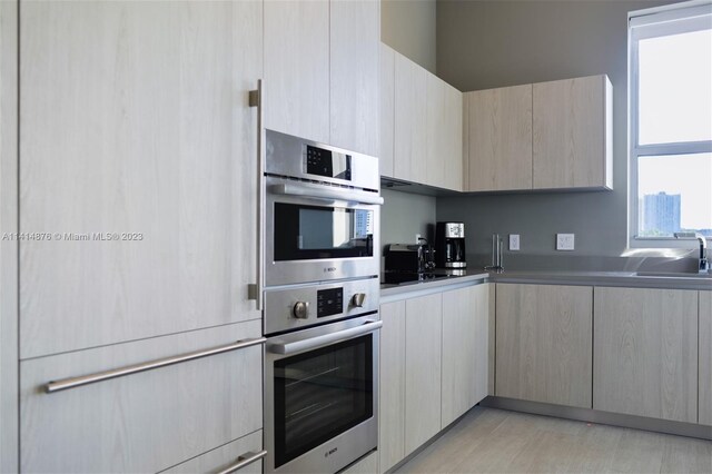 kitchen with light brown cabinetry, double oven, sink, and light hardwood / wood-style flooring