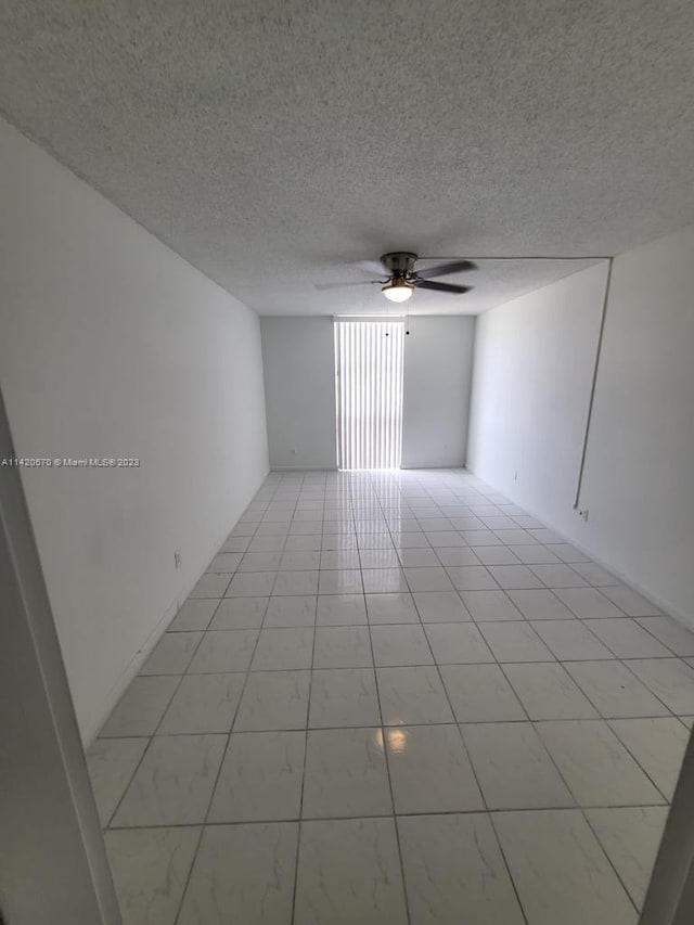 tiled empty room with ceiling fan and a textured ceiling