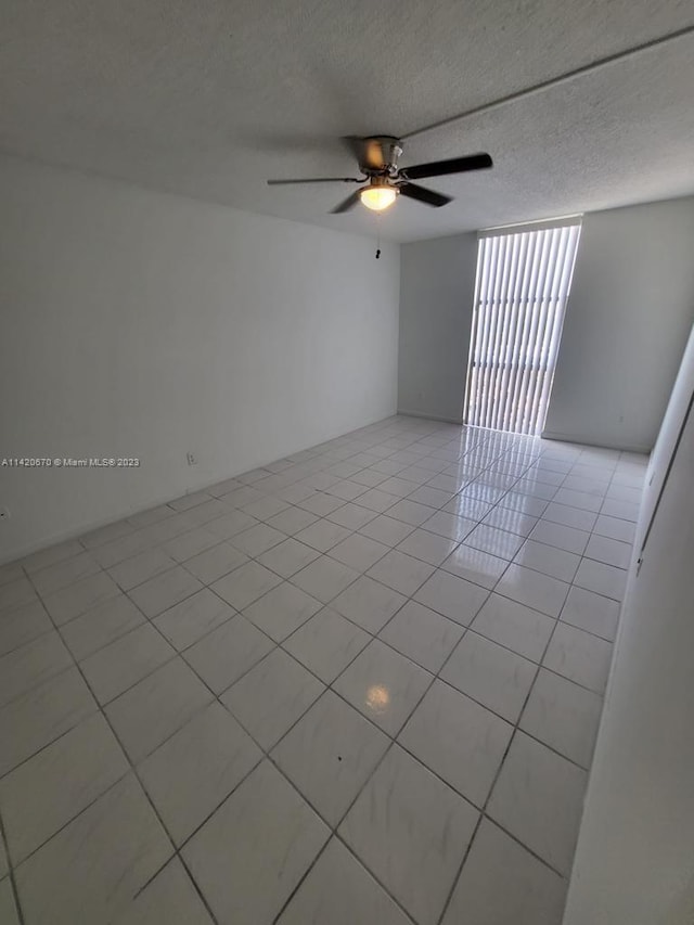 empty room with light tile floors, ceiling fan, and a textured ceiling