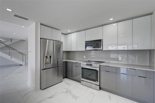 kitchen featuring white cabinetry, stainless steel appliances, gray cabinets, tasteful backsplash, and light tile floors