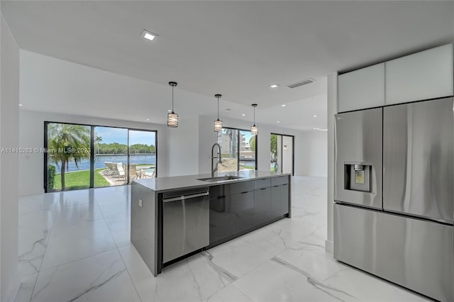 kitchen with a center island with sink, stainless steel appliances, white cabinets, a water view, and sink