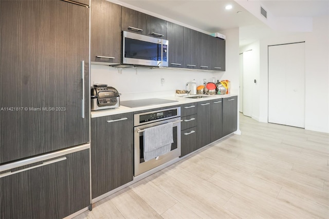 kitchen with dark brown cabinets, sink, appliances with stainless steel finishes, and light wood-type flooring