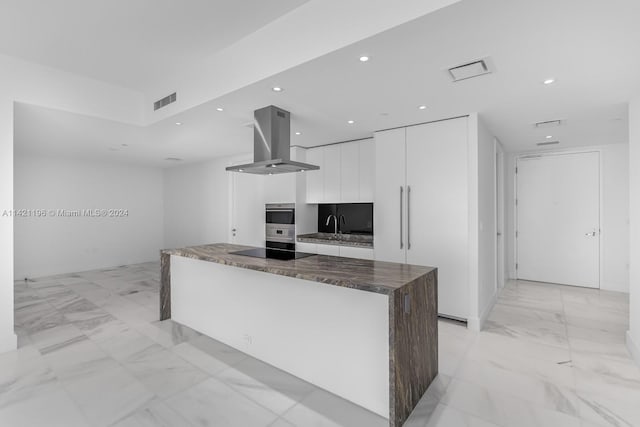 kitchen featuring a kitchen island, black electric cooktop, island exhaust hood, light tile patterned flooring, and white cabinetry