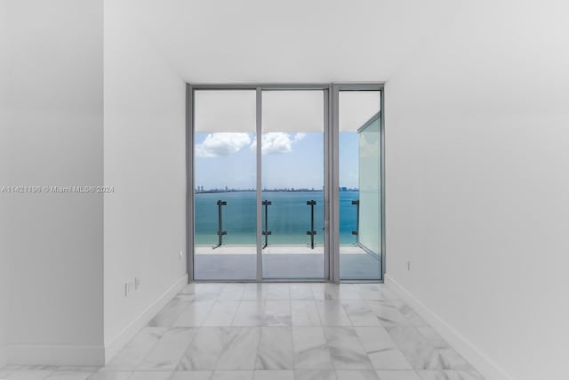 spare room featuring light tile patterned floors, a water view, a wealth of natural light, and a wall of windows