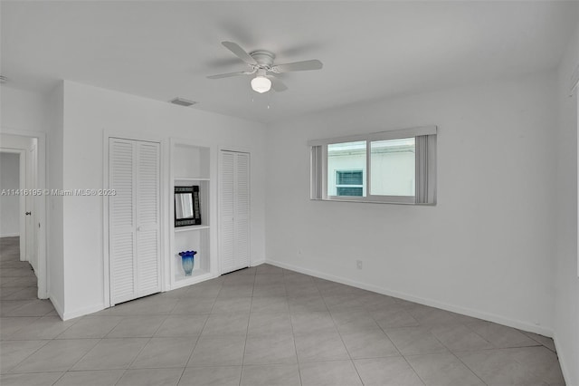 unfurnished room with light tile flooring, built in shelves, and ceiling fan