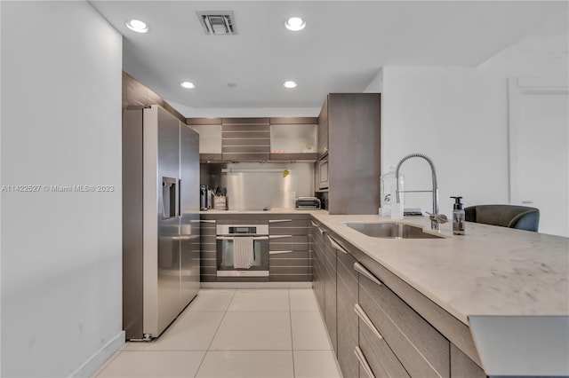 kitchen with light tile flooring, light stone counters, wall chimney exhaust hood, sink, and appliances with stainless steel finishes