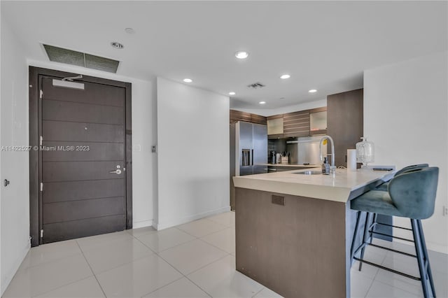 kitchen featuring a breakfast bar area, kitchen peninsula, stainless steel refrigerator with ice dispenser, sink, and light tile floors