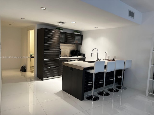 kitchen featuring a center island with sink, a kitchen bar, light tile flooring, and sink