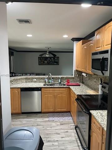 kitchen featuring light hardwood / wood-style floors, appliances with stainless steel finishes, light stone counters, sink, and tasteful backsplash