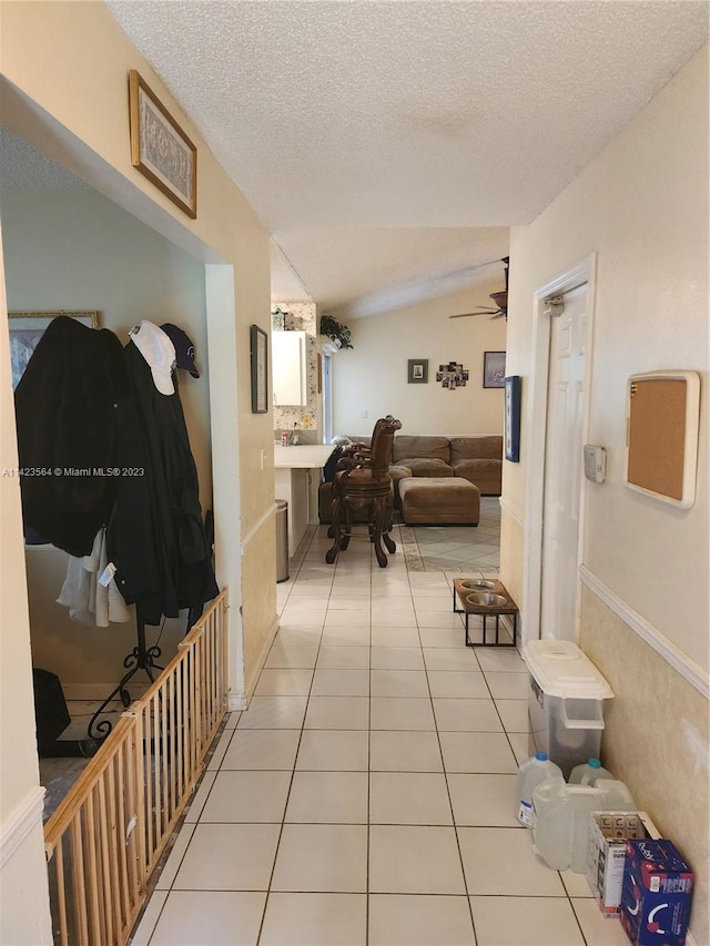 corridor featuring light tile patterned flooring, a textured ceiling, and vaulted ceiling