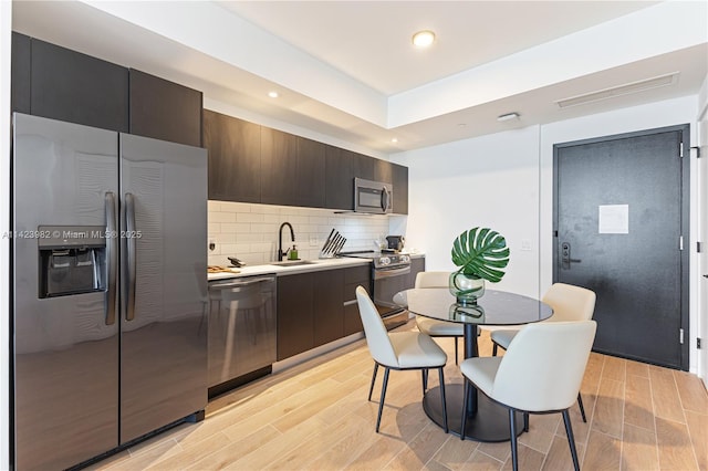 kitchen featuring sink, dark brown cabinets, stainless steel appliances, tasteful backsplash, and light wood-type flooring