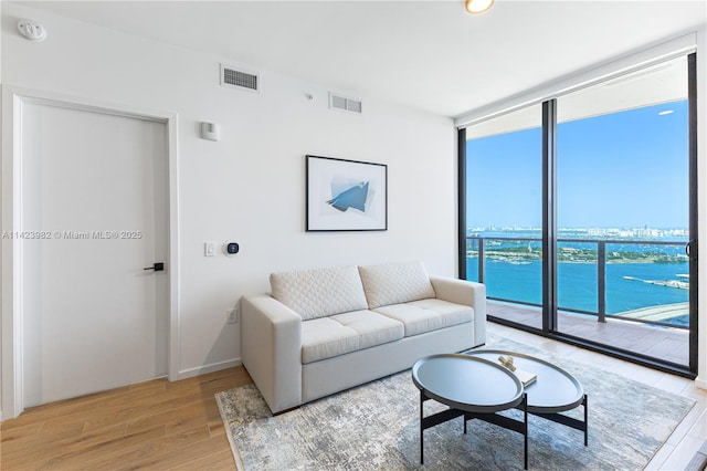 living room with hardwood / wood-style flooring, a water view, and a wall of windows