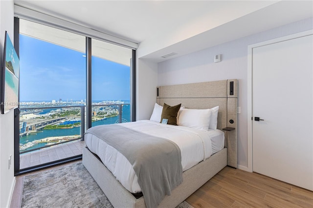 bedroom featuring a water view, floor to ceiling windows, and light hardwood / wood-style flooring