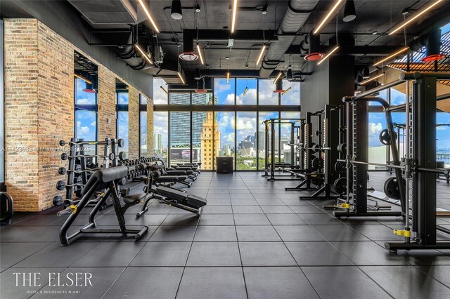 exercise room with floor to ceiling windows and brick wall