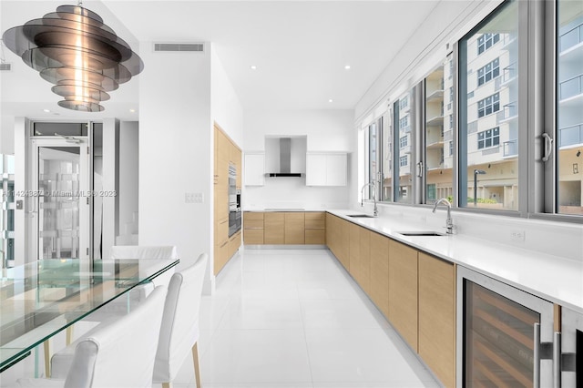 kitchen with wall chimney exhaust hood, light tile patterned floors, sink, and wine cooler