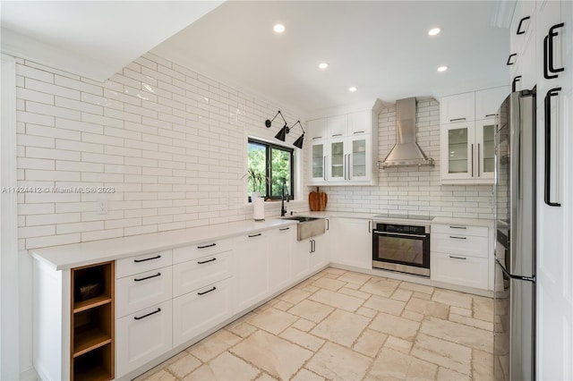 kitchen featuring appliances with stainless steel finishes, backsplash, white cabinetry, sink, and wall chimney range hood