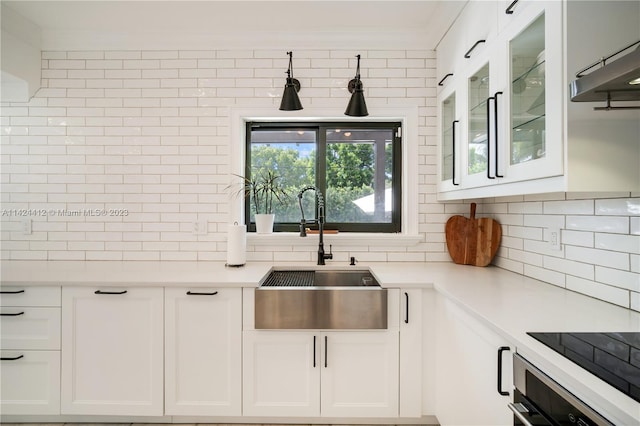 kitchen with cooktop, sink, tasteful backsplash, white cabinetry, and oven