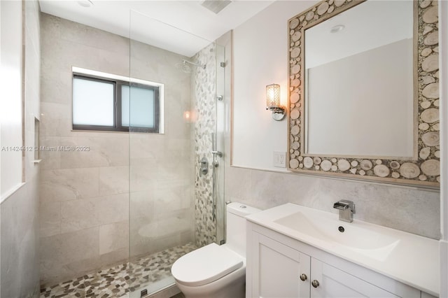 bathroom featuring tile walls, a shower with door, toilet, and vanity