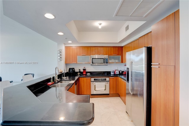 kitchen featuring kitchen peninsula, light tile flooring, appliances with stainless steel finishes, sink, and a raised ceiling